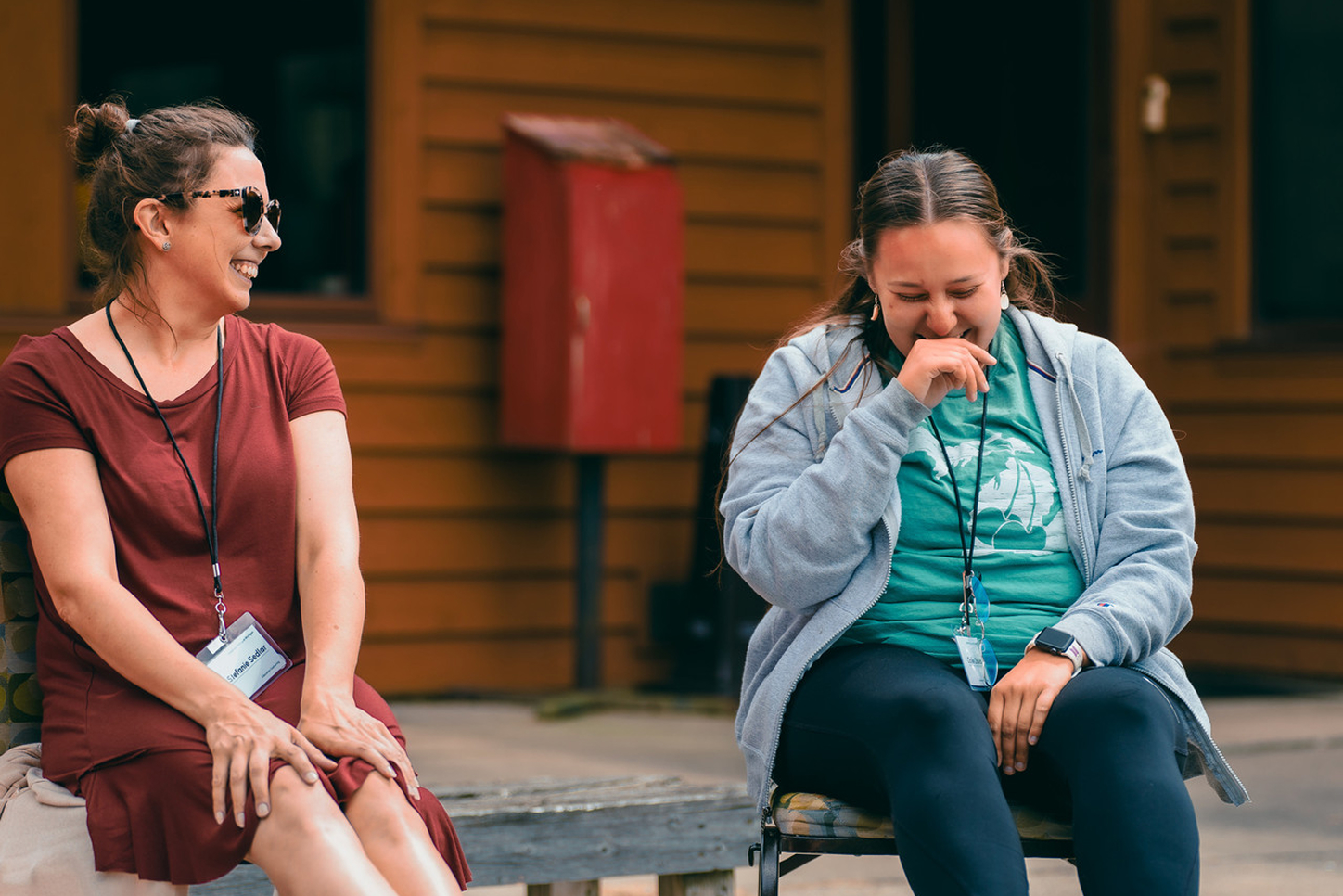 Two educators sit on a bench laughing together.